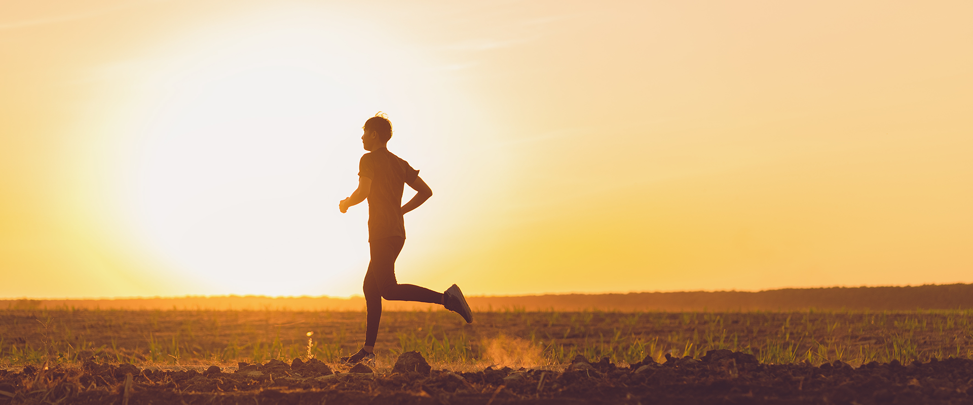 Silhouette of a man running across an open field in profile against a bright, golden sunset sky.